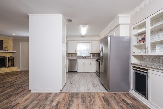 kitchen featuring wine cooler, a sink, appliances with stainless steel finishes, a brick fireplace, and crown molding