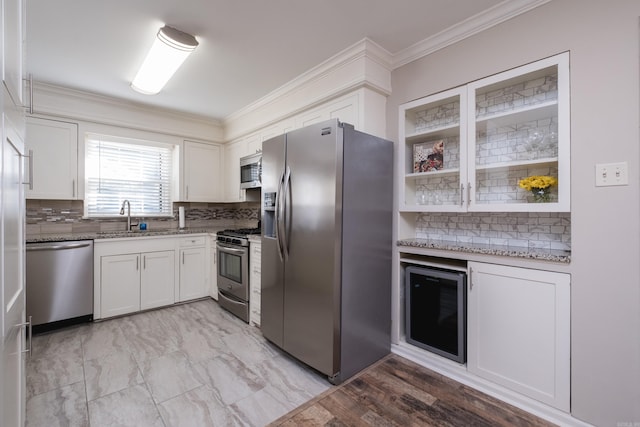 kitchen featuring stainless steel appliances, a sink, white cabinetry, light stone countertops, and crown molding