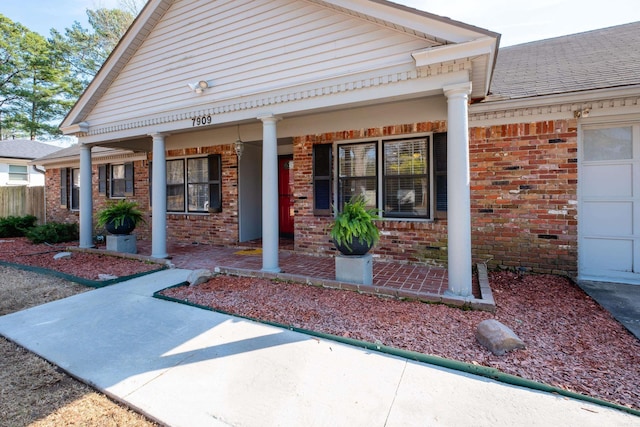 entrance to property featuring a porch, brick siding, an attached garage, and roof with shingles