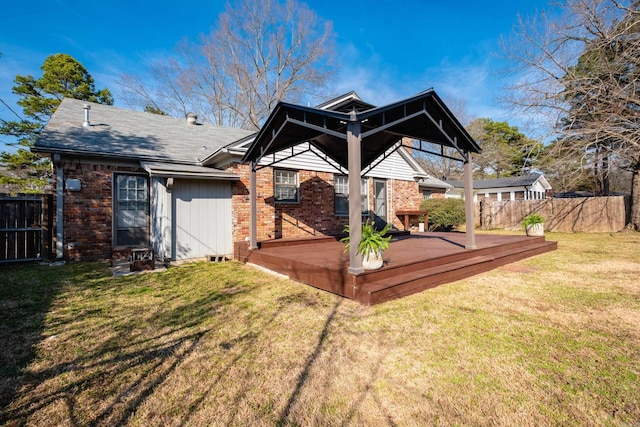 rear view of property featuring a wooden deck, fence, a lawn, and brick siding