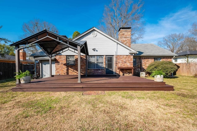 rear view of house with brick siding, a yard, a chimney, fence, and a deck