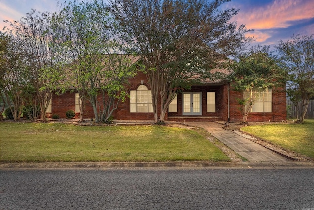 view of front facade featuring french doors, brick siding, and a lawn