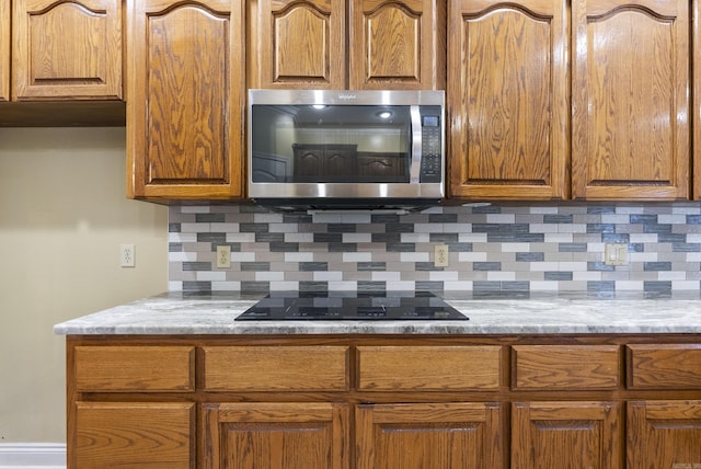 kitchen featuring black electric stovetop, stainless steel microwave, backsplash, and brown cabinets