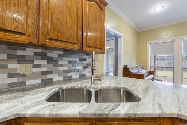 kitchen with crown molding, a sink, backsplash, and light stone countertops