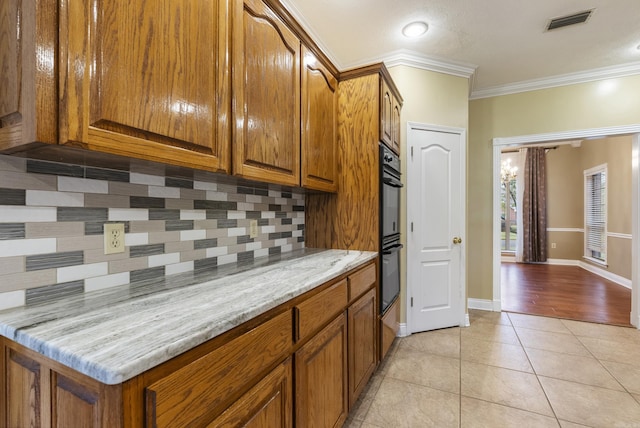 kitchen featuring light tile patterned floors, visible vents, tasteful backsplash, brown cabinetry, and crown molding