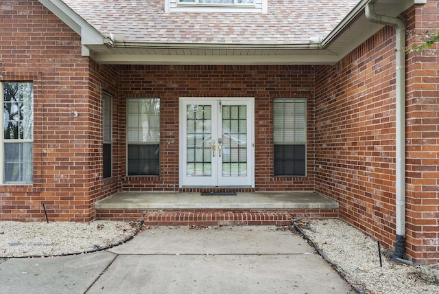 doorway to property featuring french doors, roof with shingles, and brick siding