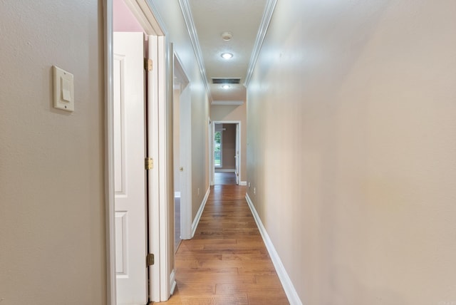 hallway featuring ornamental molding, light wood-type flooring, visible vents, and baseboards