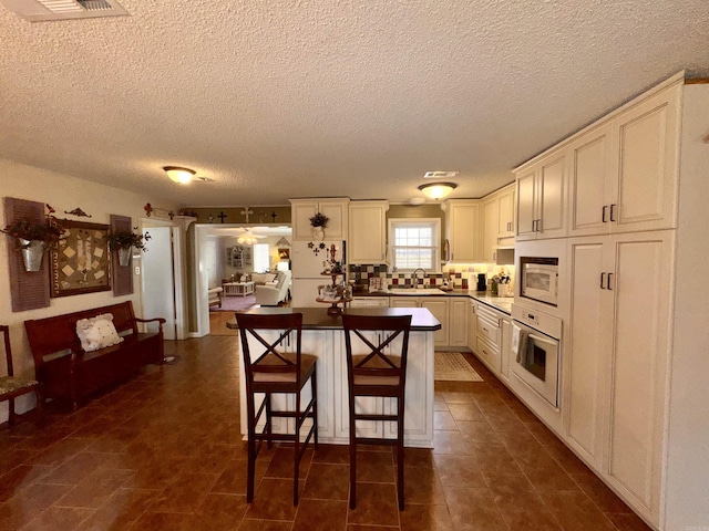 kitchen featuring white appliances, a sink, visible vents, tasteful backsplash, and a kitchen bar