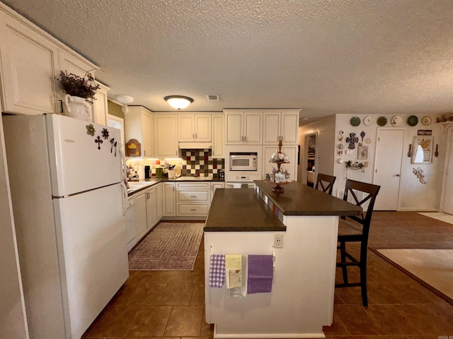 kitchen with a breakfast bar, a center island, dark countertops, white cabinets, and white appliances