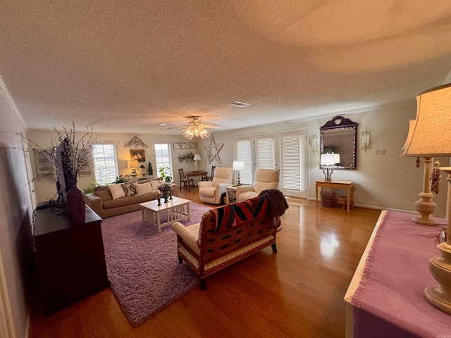 living room with a textured ceiling, ceiling fan, wood finished floors, visible vents, and crown molding