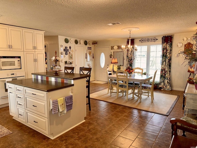 kitchen with white appliances, white cabinets, dark countertops, a kitchen island, and a chandelier