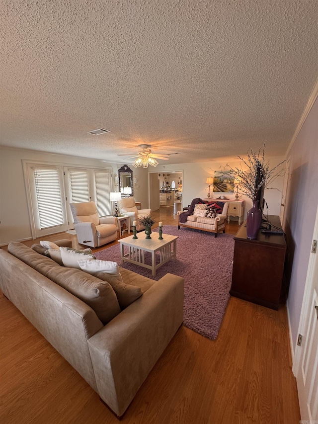 living room featuring ceiling fan, a textured ceiling, visible vents, and wood finished floors