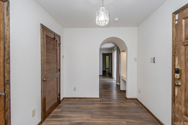 hallway with arched walkways, baseboards, and wood finished floors