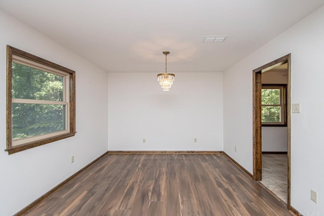 unfurnished room featuring baseboards, visible vents, a chandelier, and wood finished floors