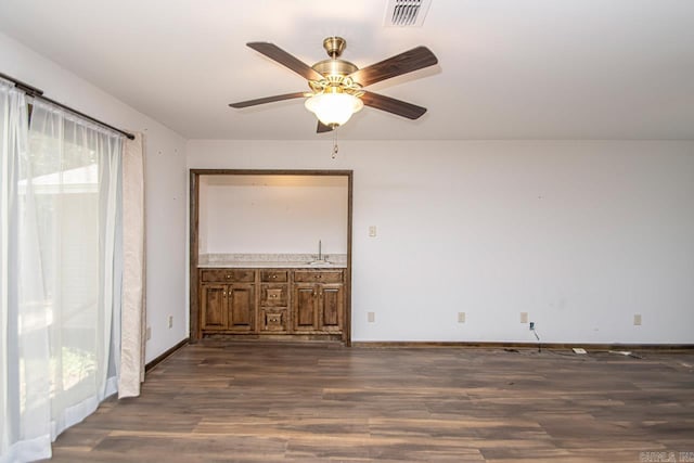 spare room featuring ceiling fan, dark wood-type flooring, a sink, visible vents, and baseboards