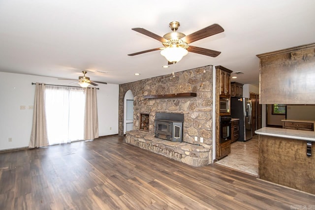 unfurnished living room with baseboards, arched walkways, ceiling fan, wood finished floors, and a wood stove