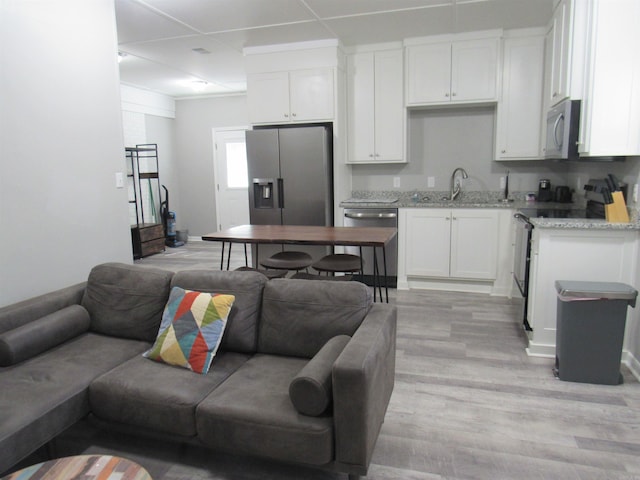 kitchen featuring stainless steel appliances, light wood-style floors, open floor plan, white cabinetry, and a sink