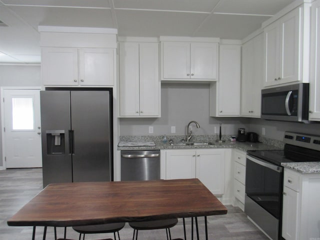 kitchen featuring stainless steel appliances, light wood finished floors, a sink, and white cabinetry