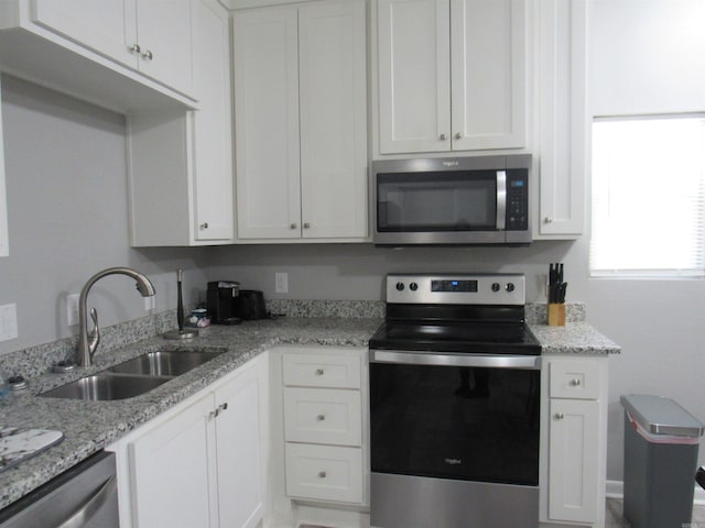 kitchen featuring appliances with stainless steel finishes, white cabinets, a sink, and light stone countertops