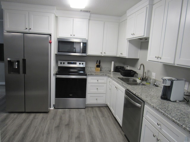 kitchen featuring stainless steel appliances, white cabinetry, a sink, light stone countertops, and light wood-type flooring