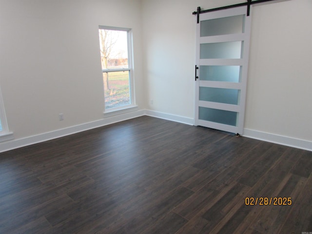 empty room with a barn door, dark wood-type flooring, and baseboards