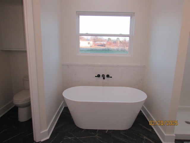 bathroom featuring toilet, a soaking tub, baseboards, and marble finish floor