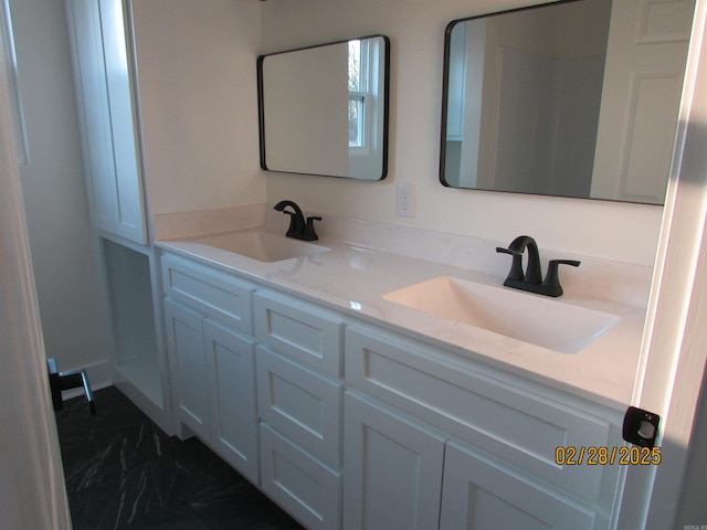 full bath featuring marble finish floor, double vanity, and a sink