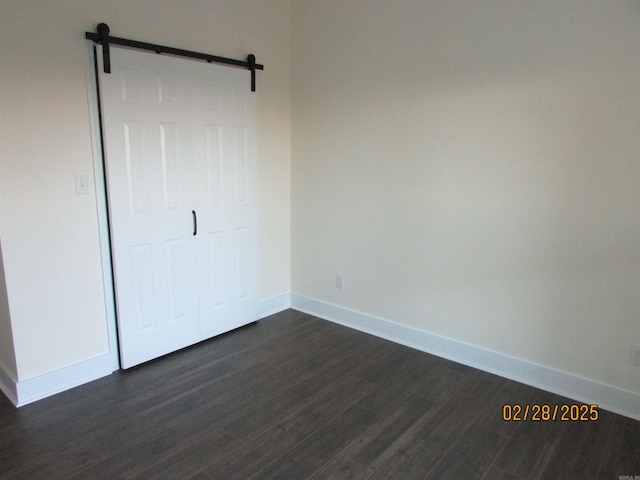 unfurnished bedroom featuring a barn door, dark wood-type flooring, and baseboards