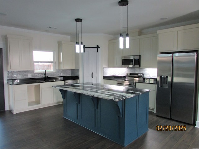 kitchen featuring a barn door, a sink, ornamental molding, appliances with stainless steel finishes, and a center island