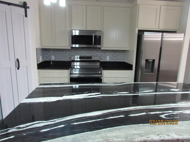 kitchen with stainless steel appliances, a barn door, white cabinetry, and tasteful backsplash