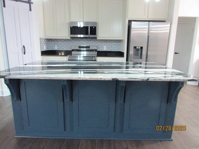 kitchen featuring appliances with stainless steel finishes, tasteful backsplash, dark wood finished floors, and a barn door