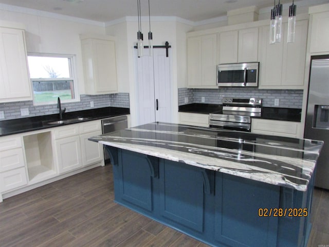 kitchen with crown molding, tasteful backsplash, a barn door, appliances with stainless steel finishes, and a sink