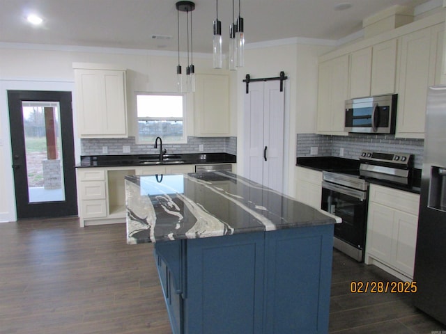 kitchen with a center island, a barn door, appliances with stainless steel finishes, ornamental molding, and a sink