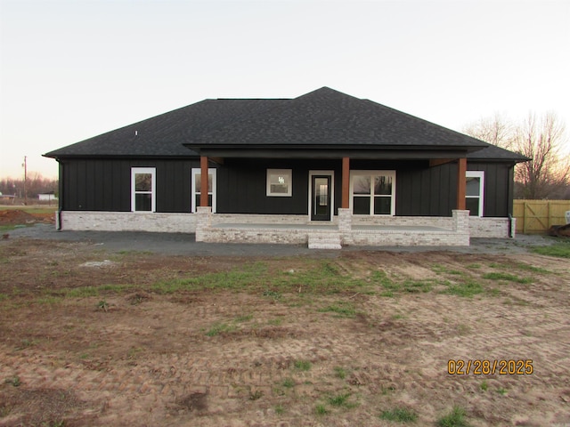 rear view of property with a shingled roof, a porch, and board and batten siding