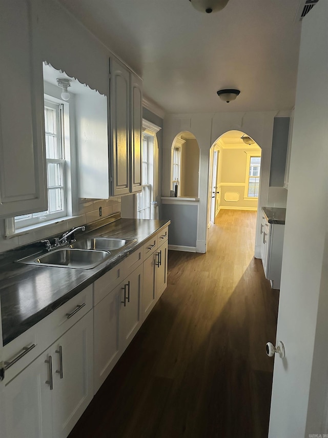 kitchen featuring arched walkways, dark countertops, visible vents, dark wood-type flooring, and a sink