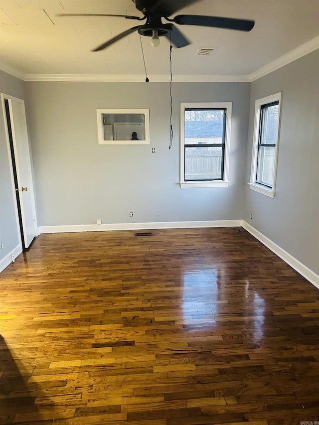 spare room featuring dark wood-type flooring, visible vents, crown molding, and baseboards