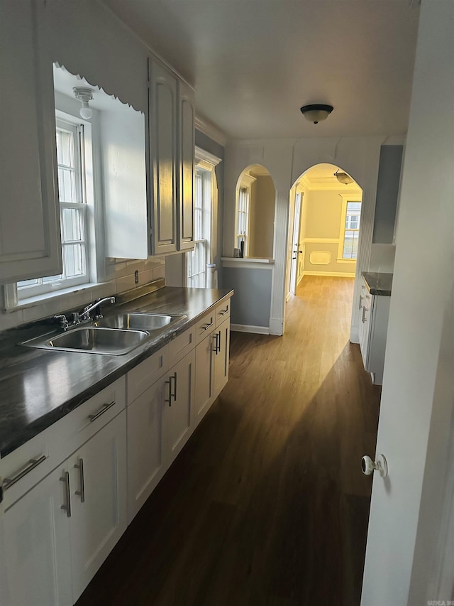 kitchen featuring arched walkways, dark wood-style flooring, a sink, white cabinetry, and dark countertops