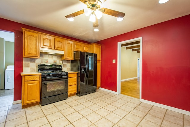 kitchen featuring under cabinet range hood, light countertops, black appliances, tasteful backsplash, and washer / dryer