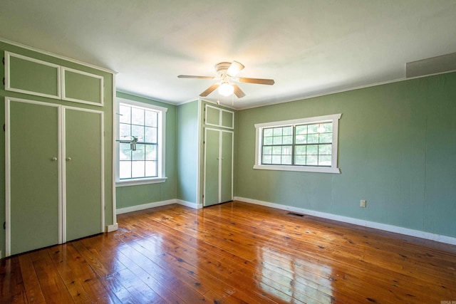 unfurnished bedroom with ornamental molding, visible vents, baseboards, and hardwood / wood-style flooring