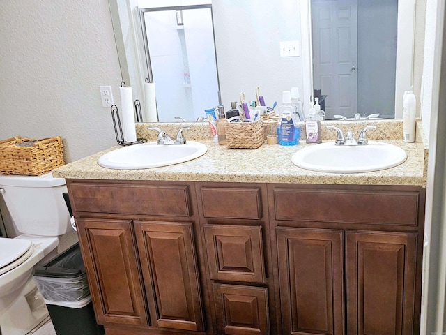 full bathroom with a textured wall, a sink, toilet, and double vanity