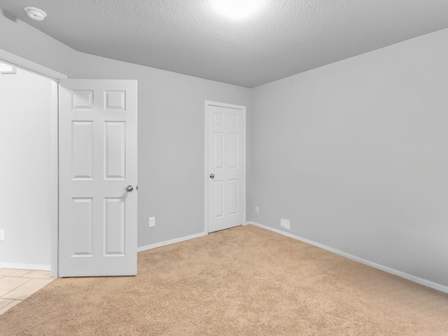 unfurnished bedroom with light carpet, light tile patterned floors, baseboards, and a textured ceiling