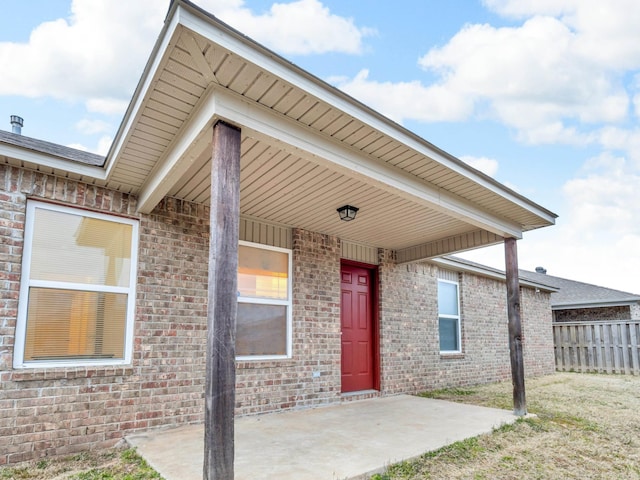 property entrance featuring brick siding, fence, and a patio