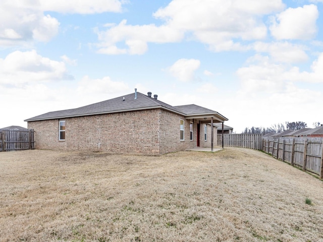 rear view of property featuring brick siding, a lawn, and a fenced backyard