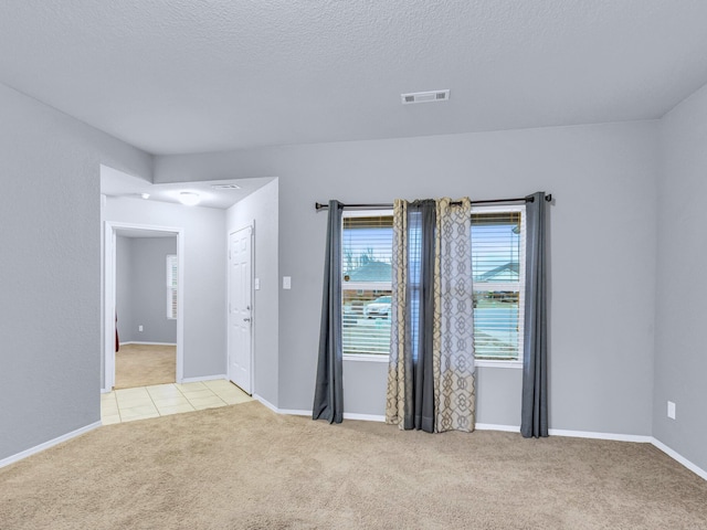 unfurnished room featuring light carpet, a textured ceiling, visible vents, and baseboards