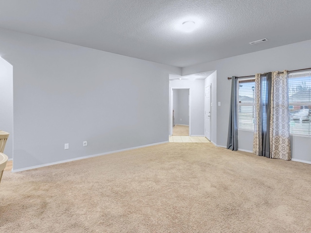 empty room featuring light carpet, a textured ceiling, visible vents, and baseboards