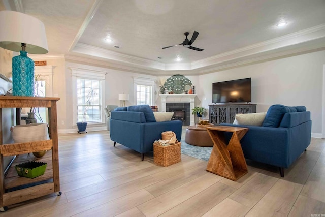 living room featuring ornamental molding, light wood finished floors, a tiled fireplace, and a raised ceiling