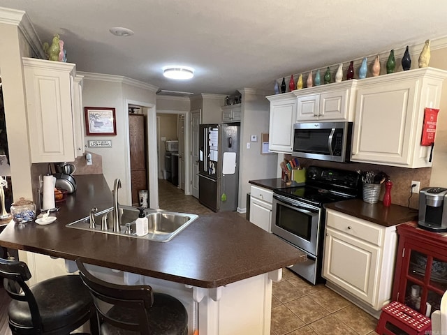 kitchen featuring light tile patterned floors, dark countertops, appliances with stainless steel finishes, a sink, and a peninsula