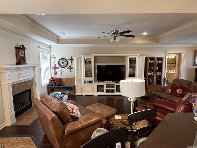 living area with a fireplace, ornamental molding, a raised ceiling, and wood finished floors