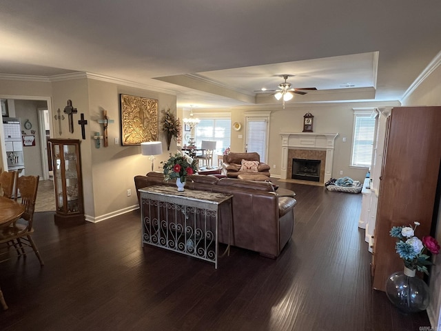 living room featuring dark wood-type flooring, a tile fireplace, a raised ceiling, and crown molding