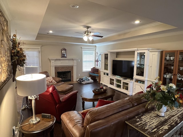 living room featuring ceiling fan, wood finished floors, a tray ceiling, a tiled fireplace, and crown molding